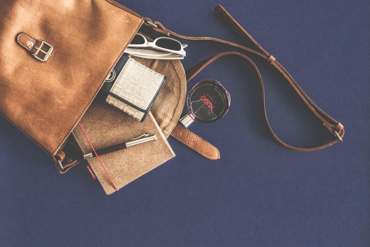 home-hero Stylish flat lay of a leather handbag with luxury accessories including sunglasses, wallet, notebook, and pen.